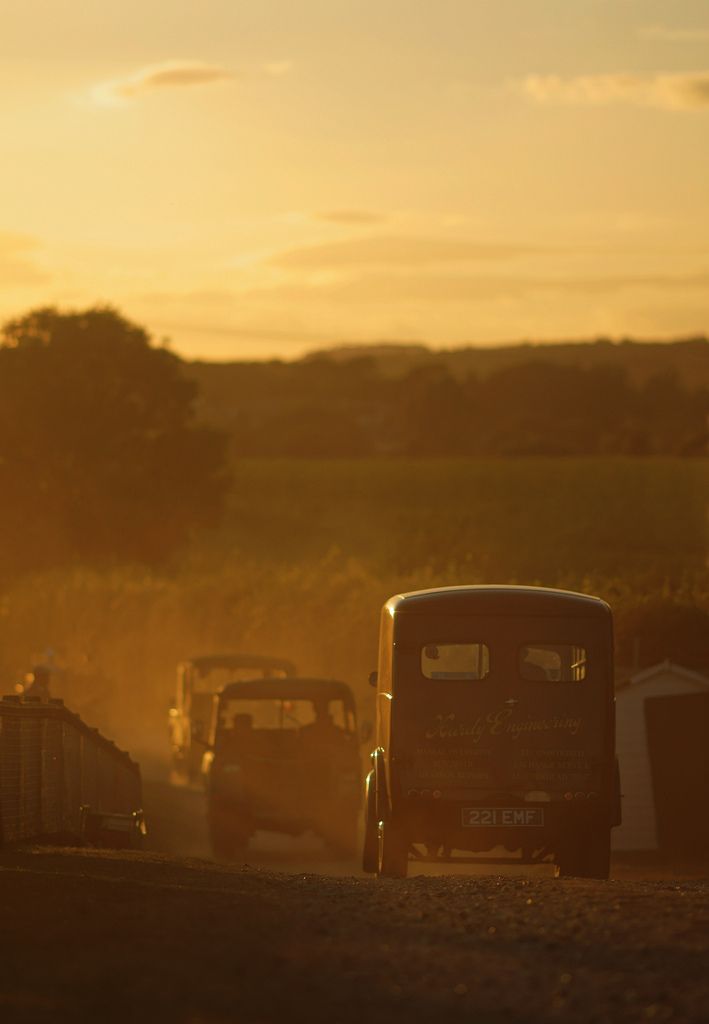 Old vehicles travelling down a dusty country lane late one glorious summer evening.